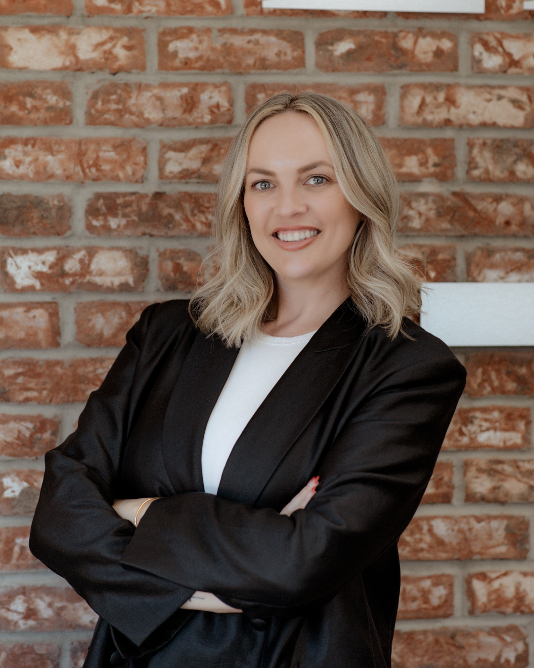 Kira Conkle, licensed aesthetician and office manager at Avesta Aesthetics, smiling confidently against a brick wall, showcasing her expertise in personalized skincare treatments.